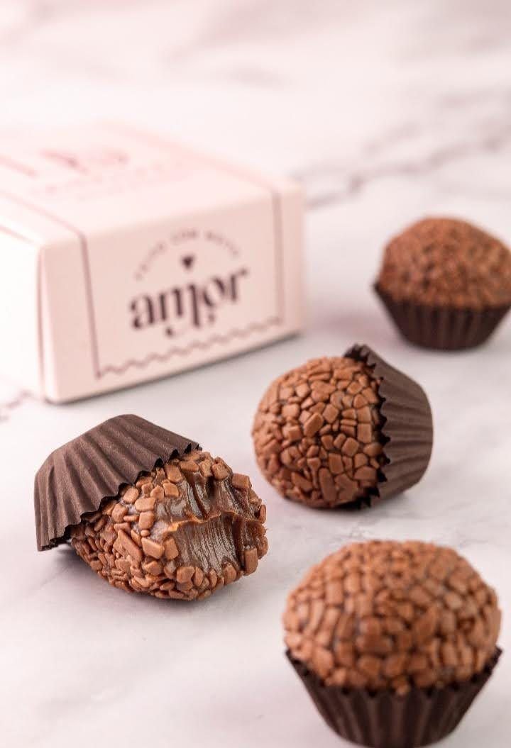 Brigadeiros de chocolate com granulado ao lado de uma caixa rosa