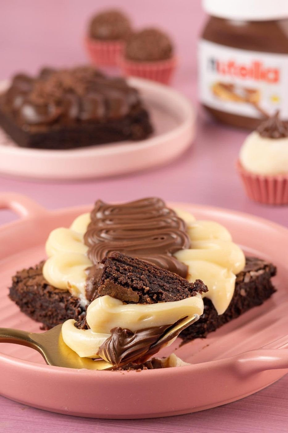 Brownie com creme branco e brigadeiro sendo cortado com garfo dourado